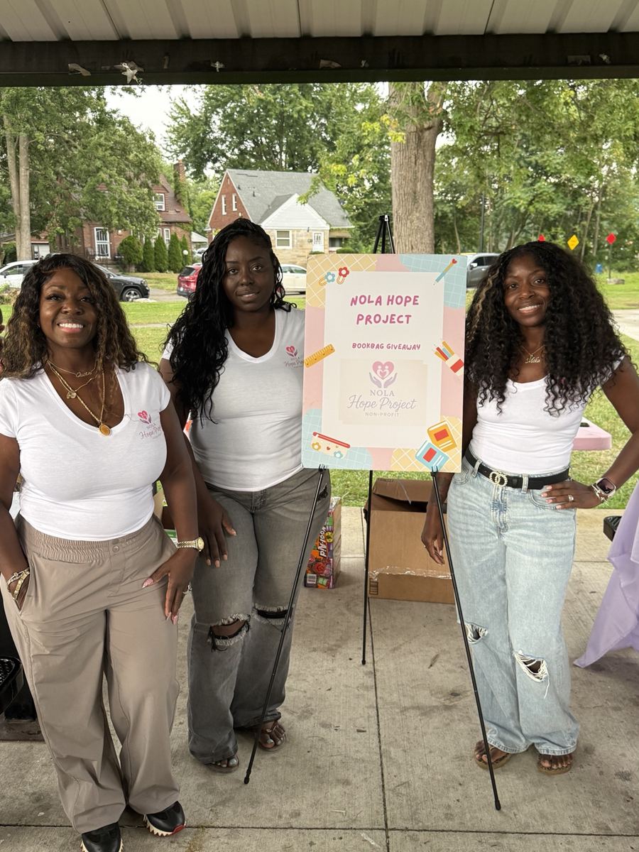 Three community event team members beside the Nola Hope Project bookbag giveaway sign
